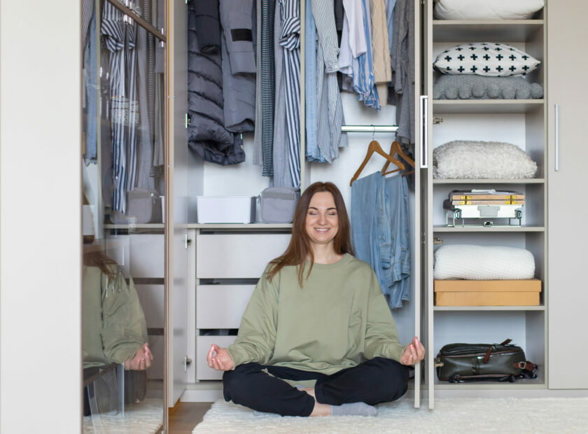 Cheerful female in lotus position at modern wardrobe storage. Happy housewife posing meditating